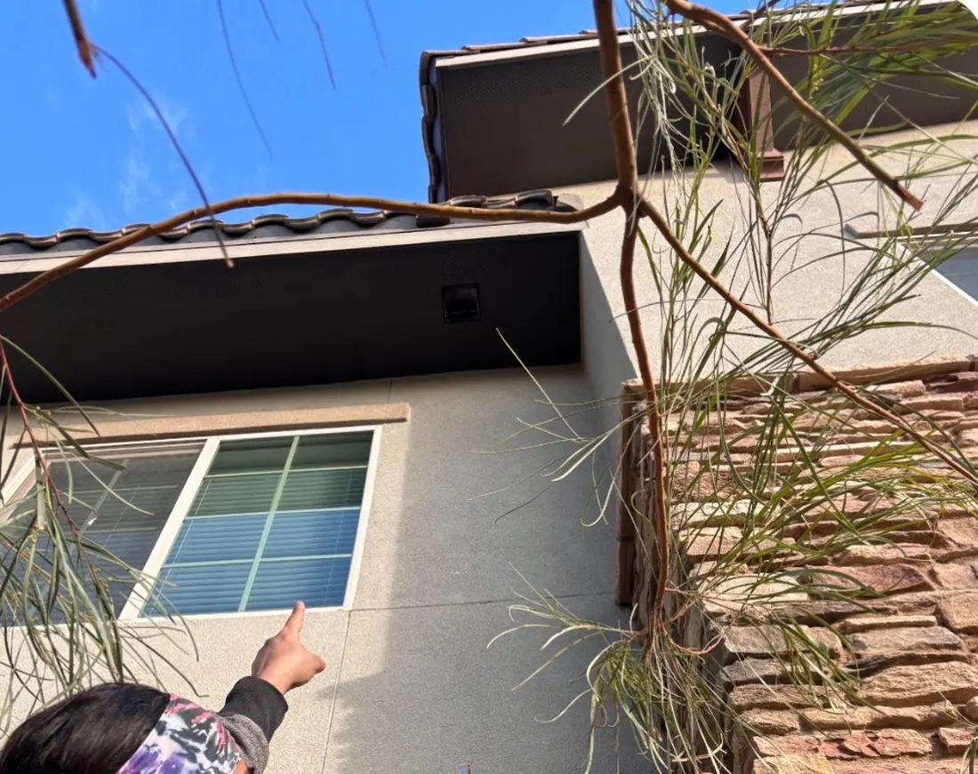 Pointing out a second-story dryer vent termination on a building exterior