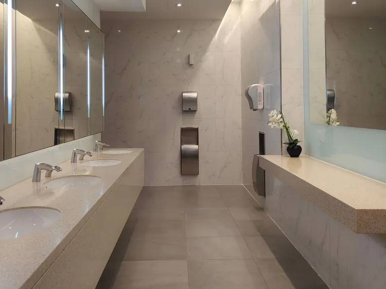 Clean commercial restroom with a row of sinks, stone counters, and tile floor